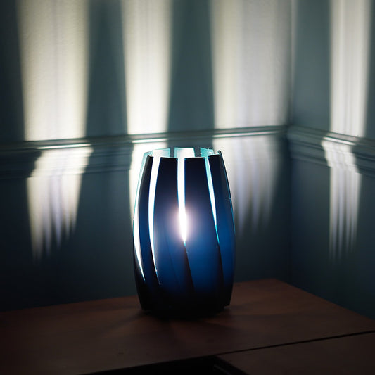 A blue upright lamp with blades-like design, casting a shadow on the wall in a dark room.