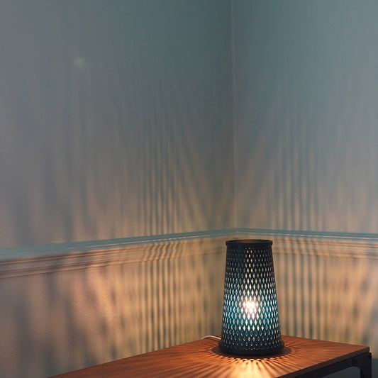 A tall, cylindrical lamp with a geometric pattern casting a shadow on a wall.