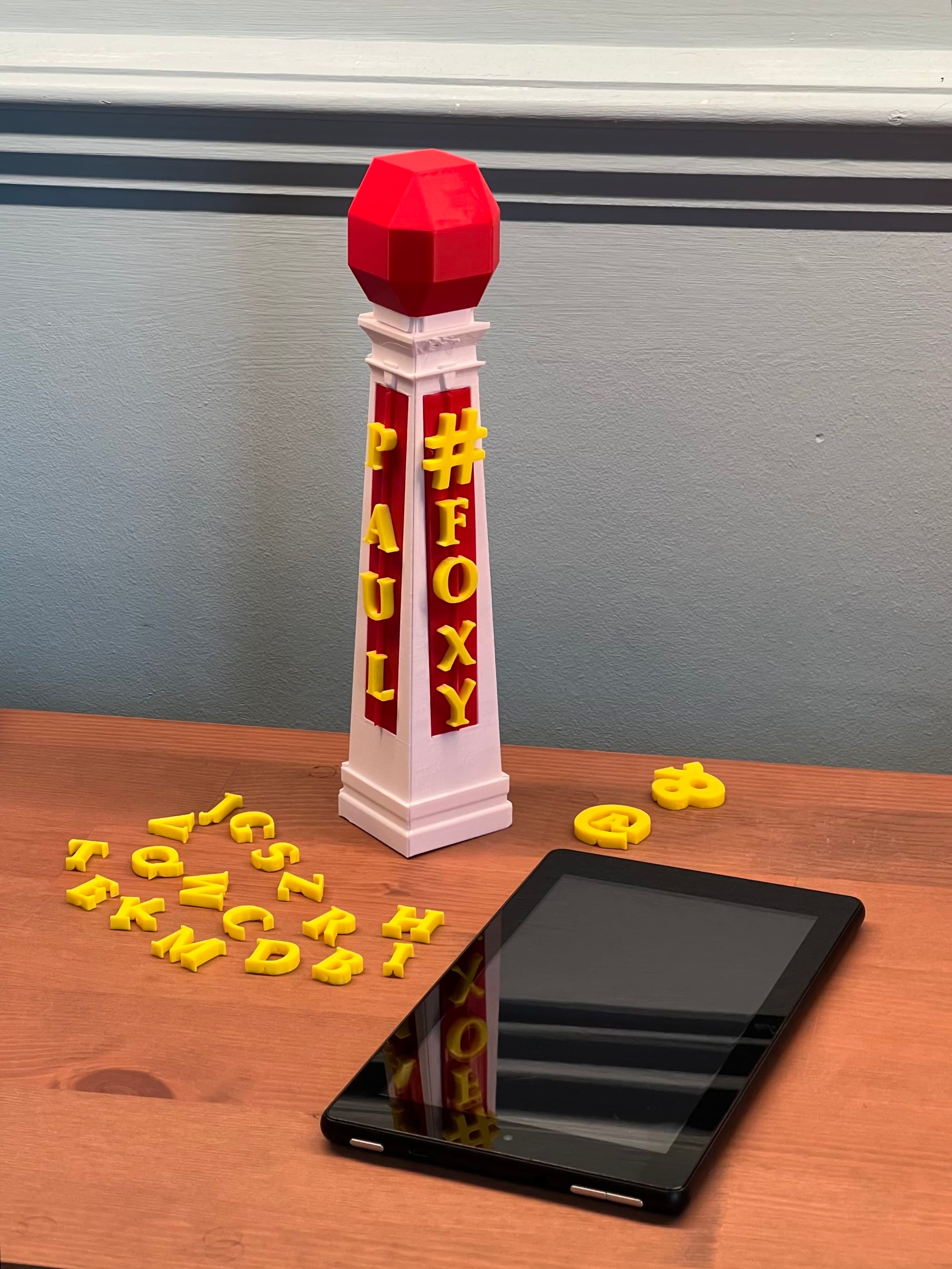 A toy model of a Lido sign with snap-on letters, featuring a red and yellow ball on top, placed next to a smartphone for scale.