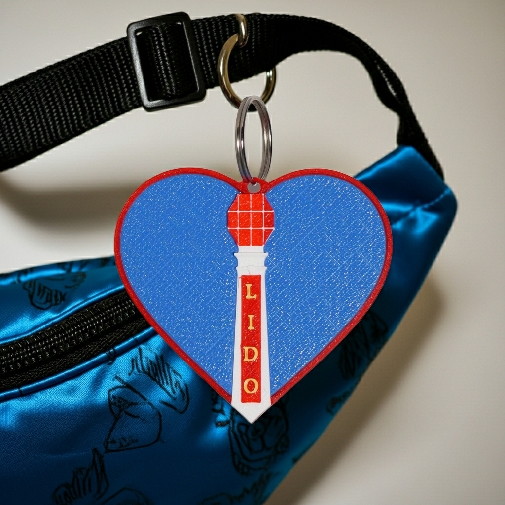 Heart-shaped keychain with a tower design and 'LIDO' text on a blue bag.